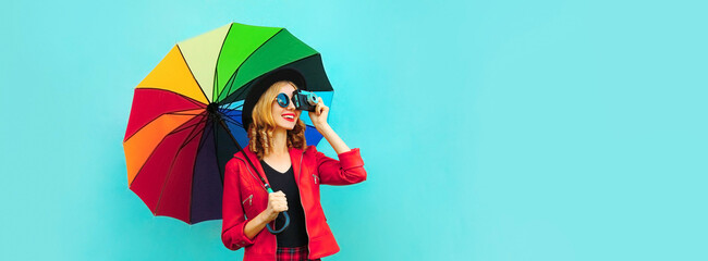 Wall Mural - Portrait of happy smiling young woman photographer with film camera and colorful umbrella on blue background, blank copy space for advertising text