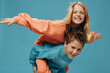© Tatiana - happy joyful children, brother and sister of school age play together and the boy rolls the girl on his back. Horizontal studio photography on a blue background