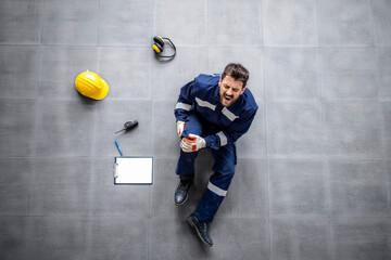 Wall Mural - Top view of an injured factory worker having broken knee pain due to fall. Safety at work.