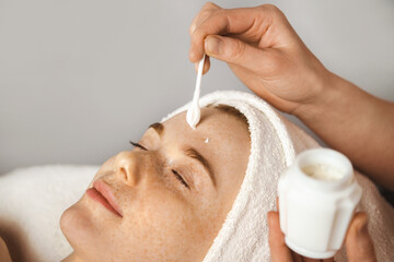 Wall Mural - close up portrait woman with closed eyes receiving facial rejuvenation procedure with cream in spa s