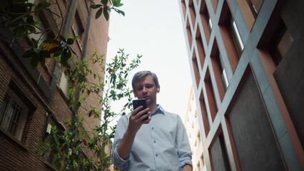 Young man tourist using smartphone close-up, businessman in headphones writing message in phone, standing in street. Guy chatting with friends online, surfing the internet. 