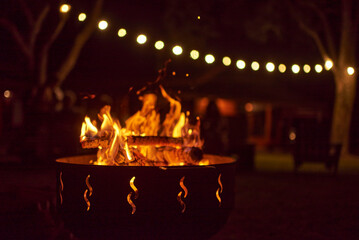 Bonfire burning in a garden on a warm summer night, unrecognizable people in the background. Concepts: coziness, travel, enjoyment of the outdoors.