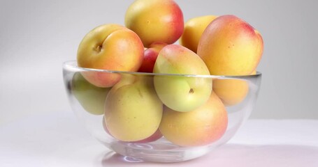 Wall Mural - Fresh ripe juicy yellow orange red apricot fruit pile whole cut half slice seed in transparent glass bowl on white background rotate turn move closeup