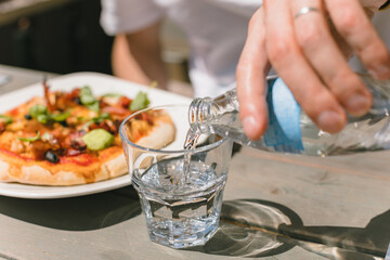 Man pouring water into glass while eating pizza outdoors. Summer lifestyle.