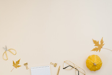 Workplace computer with yellow maple leaves and pumpkins, scissors, notepad, pen, clips, paper clips on a light beige background. Flat lay, top view. Work office desk with autumn blogger