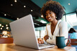 © fotofabrika - Smiling young african woman sitting with laptop in cafe