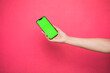 Leinwandbild Motiv Woman hand Holding a Green Screen Smartphone on pink background.