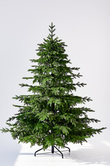 artificial christmas green tree without decorations on a metal stand isolated on a white background.