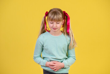 Little girl with stomach ache against yellow background
