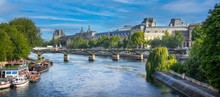 Panoramic View Of The Pont Des Arts In Paris With The Louvre Museum Behind The Bridge Over The Seine River That Divides Paris In Two Parts Under A Sky Blue Sky And On A Navy Blue Water. Paris Bridge.