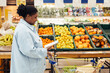 © Seventyfour - Side view portrait of black woman reading shopping list while buying groceries in supermarket, copy space