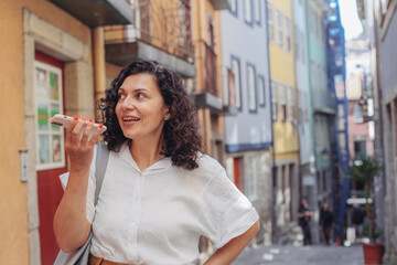 Woman recording an audio message, using her smartphone, walking on an old European street