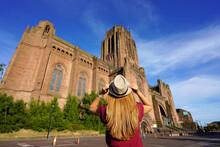 Back View Of Tourist Girl Looking The Cathedral Church Of Christ Against Blue Sky In Liverpool On Sunset, United Kingdom