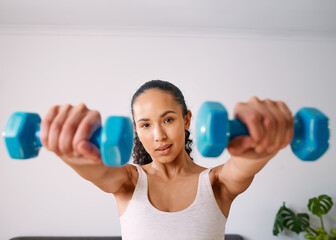 A serious young woman lifts small weights to get strong at home