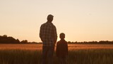 Farmer and his son in front of a sunset agricultural landscape. Man and a boy in a countryside field. Fatherhood, country life, farming and country lifestyle.