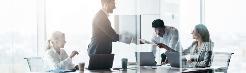 Wall Mural - Team of young businessmen working and communicating together in office. Blurred background
