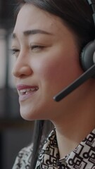 Wall Mural - Vertical video: Close up of call center employee with headphones talking on phone call about telemarketing with clients. Woman using microphone for telecommunication with people at customer support.