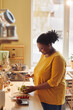 © Seventyfour - Vertical portrait of overweight black woman cooking healthy meal in kitchen lit by sunlight
