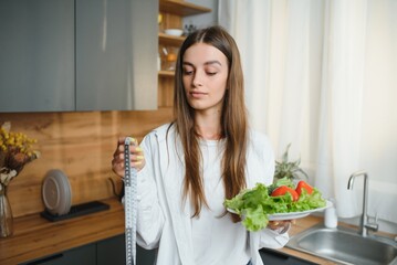 Wall Mural - Happy young woman preparing salad in kitchen. Healthy diet