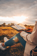 Christian Woman Holds Bible In Her Hands. Reading The Holy Bible In A Field During Beautiful Sunset. Concept For Faith, Spirituality And Religion. Peace, Hope