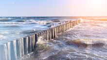 Seaside Of Baltic Sea In Poland. Seagulls Over Stormy Sea, With Waves Hiting Wooden Poles. Windy Day With Blue Sky, Sunset With Sun Flare. Lines Of Wooden Poles Protect Beach Working As Wave Breakers