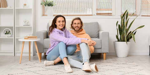 Happy young couple sitting on soft carpet at home