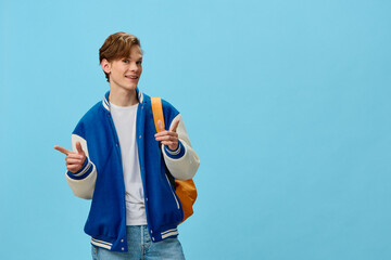 happy, attractive young man student in fashionable bomber jacket and with a bright backpack on his back stands on a blue background and spreads his arms to the sides.Horizontal photo with empty space