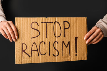 Wall Mural - Hands holding piece of carton with text STOP RACISM on dark background