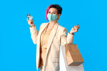 Poster - Beautiful woman in medical mask with credit card and shopping bags on blue background