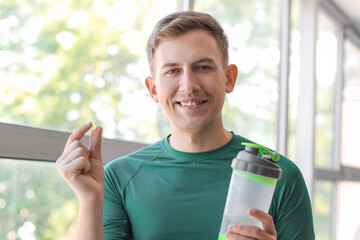 Wall Mural - Young man with vitamin supplement and bottle of water near window