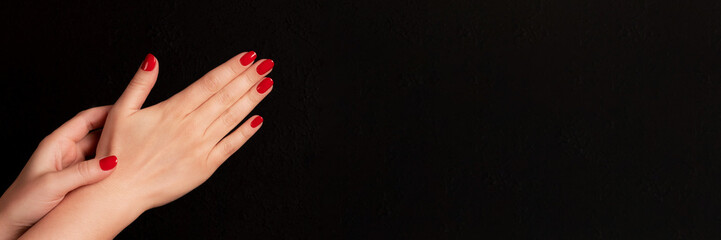 Wall Mural - Female hands with beautiful manicure - red nails on dark black background with copy space banner. Wide panoramic header