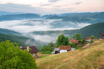 Wall Mural - Amazing view with small mountain huts against the background of beautiful low clouds creeping among the mountain slopes, Rhodopes in Bulgaria at sunrise