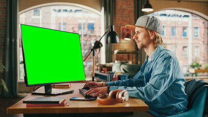 Poster - Young Handsome Man Working from Home on Desktop Computer with Green Screen Mock Up Display. Student Making Homework Assignment, Studying for Exams. Urban City View from Big Window.
