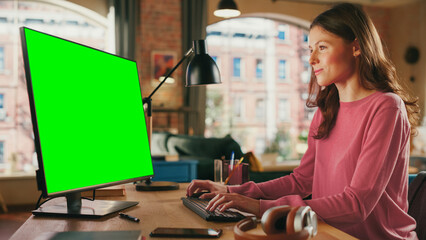 Poster - young pretty female working from home on desktop computer with green screen mock up display. creativ