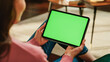 © Gorodenkoff - Female Holding Tablet Computer with Green Screen Mock Up Display. Woman Relaxing at Home, Watching Videos and Reading Social Media Posts on Mobile Device. Close Up Over the Shoulder Photo.