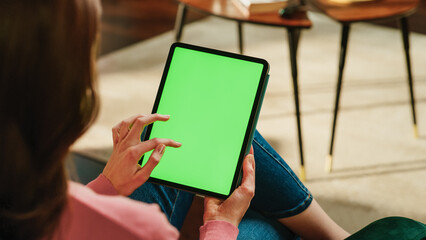 Fototapete - Female Scrolling and Tapping on Content on Tablet Computer with Green Screen Mock Up Display. Woman Relaxing at Home, Reading Social Media Posts on Mobile Device. Close Up Over the Shoulder Photo.