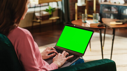 Fototapete - Young Adult Woman Working from Home Loft Apartment on Laptop Computer with Green Screen Mock Up Display. Creative Female Using Trackpad and Browsing Internet. Close Up Over the Shoulder Photo.