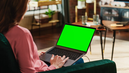 Fototapete - Young Adult Woman Working from Home Loft Apartment on Laptop Computer with Green Screen Mock Up Display. Creative Female Using Trackpad and Browsing Internet. Close Up Over the Shoulder Photo.