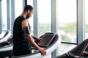 Wall Mural - Sporty Black Male Athlete Selecting Running Mode On Treadmill Before Training