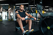 Leinwandbild Motiv Sporty Young Black Man Exercising With Rowing Machine At Modern Gym