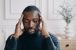 © VK Studio - Exhausted young Afro American male entrepreneur sitting with eyes closed and with hands on his head