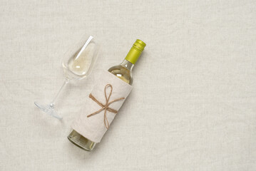 Wall Mural - White wine in a bottle and a glass flat lay on a beige textile background. View from above. Wine tasting concept.