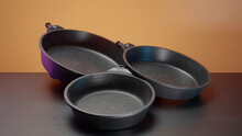 Concept Of Kitchen Utensils, Close Up Of New Set Of Frying Pans Lying On The Table. Action. New Modern Non Stick Pans.
