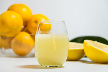 peels of yellow grapefruit squeezed next to a glass of its juice, leaves on the table