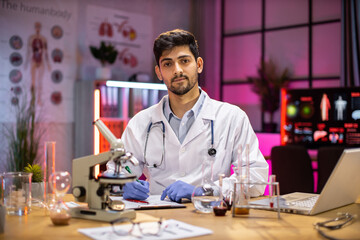 Wall Mural - Male scientist working in laboratory. Young indian man researcher supervisor are doing investigations with test tubes while writing research results