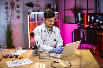 Wall Mural - Medical research laboratory: portrait of a attractive male scientist using digital laptop computer, analysing liquid biochemicals in a laboratory flask. Advanced scientific biotechnology laboratory.