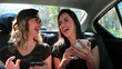 Friends laughing in the back seat of a taxi cab while looking at their cellphones sharing message