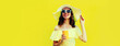 Leinwandbild Motiv Portrait of beautiful young woman drinking fresh juice wearing white summer straw hat on yellow background