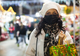 Fototapeta Uliczki - Woman in protective mask with paper shopping bags at Christmas fair