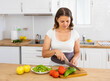 © JackF - Positive woman is cutting vegetables for salad in the kitchen at home